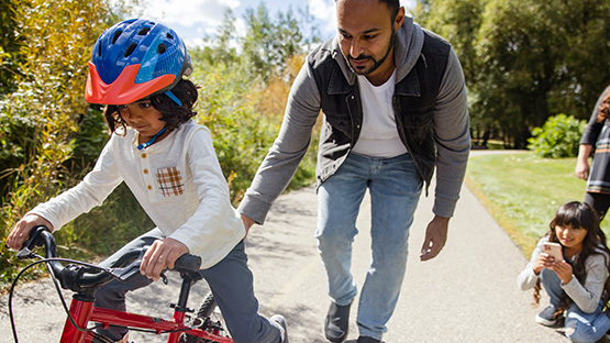 A man helping a young girl learning to ride a bike to illustrate mental health for children and adolescents.