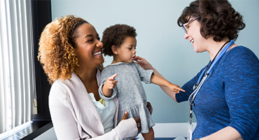 Female doctor talking with mother and toddler in examination room