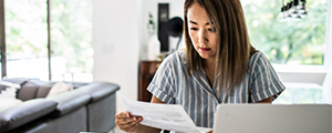 woman sitting at table reading a letter at laptop