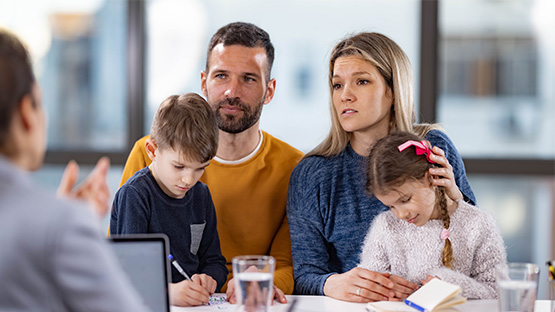 Mother and Father with their daughter and son sitting at table talking to a female doctor