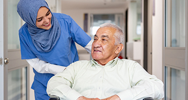 female medical person in a hijab pushing an elderly man in a wheelchair