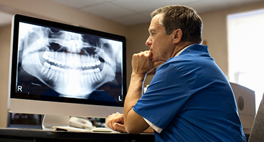 Male doctor looking at teeth x-rays on monitor