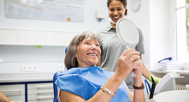 Older woman in dentist chair looking at her teeth in a hand held mirror