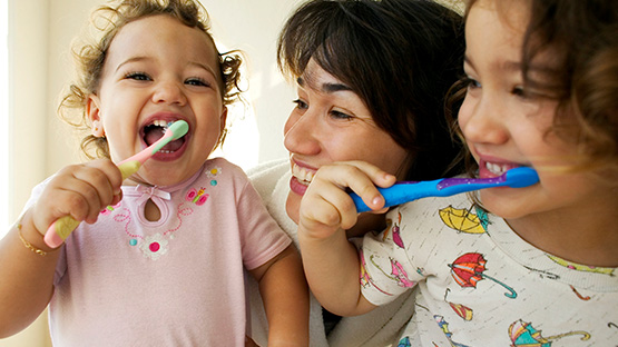Mother smiling with two toddler girls brushing their teeth