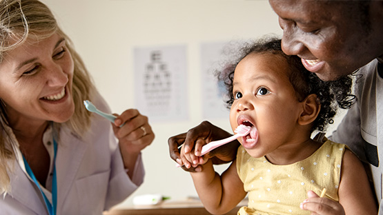 Smiling father with toddler daughter brushing her teeth and smiling dentist