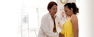 pregnant woman being examined with a stethoscope by female doctor on an examination table