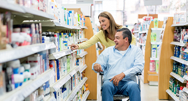 man in wheelchair with woman pushing him down the aisle in a pharmacy