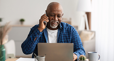 senior man sitting at table in  front of a laptop on the phone