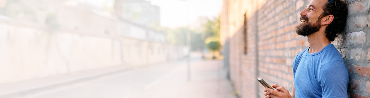 smiling man standing outside leaning up against a brick wall