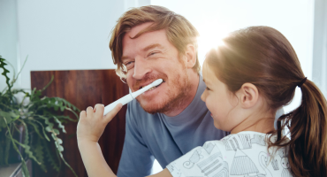 A happy adult is getting their teeth brushed by a young person.
