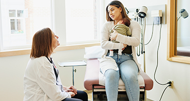 A woman is holding her baby while at a doctor's appointment. 
