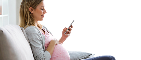 A pregnant woman is looking at her phone during a video chat.