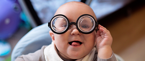 A closeup photo of a smiling infant wearing glasses. 