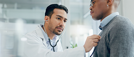 A doctor is listening to his patients chest using a stethoscope in a bright, clean medical office room. 