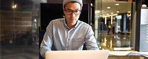 A young man is sitting in a cafe, using his laptop.