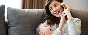 A woman is talking on the phone with her baby in her lap. Her baby is playing and trying to grab the phone from her. 